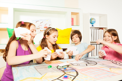 Four friends, ten years old kids, sitting at the table, playing the tabletop game with cards